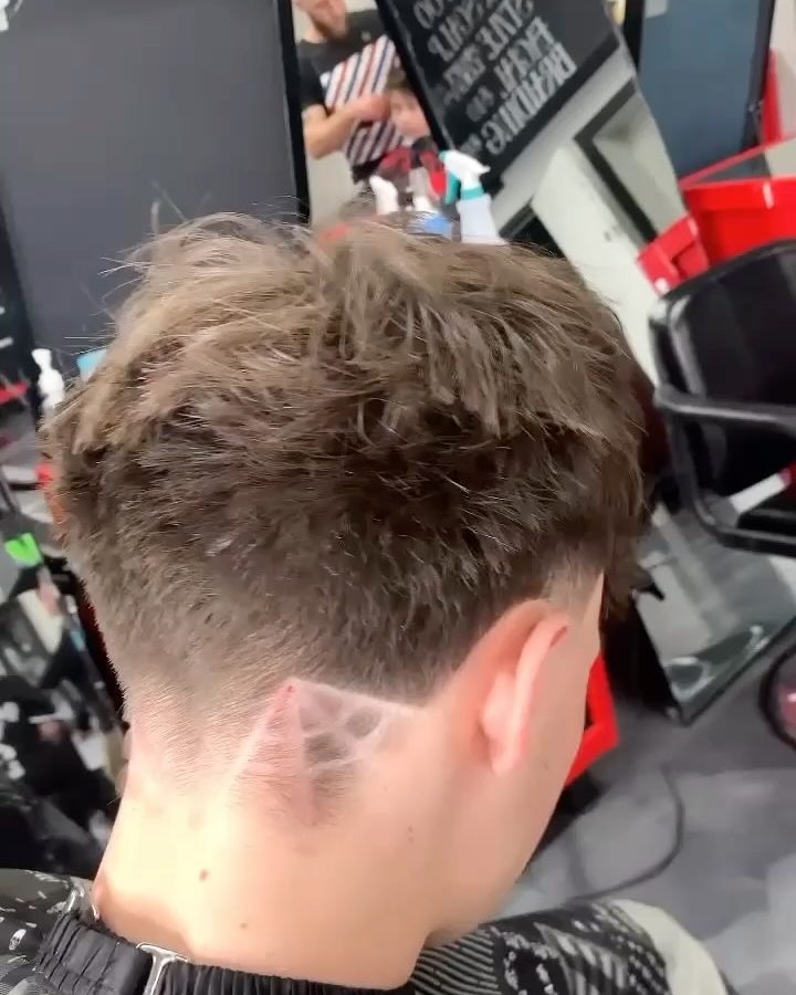 Back of a client's head showing a low taper with a spider-web design shaved in